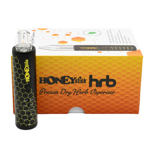 The image shows a dry herb vaporizer pen with a black body and a yellow and orange box with the HONEYstick brand on it. The vaporizer is designed for heating chamber with precision temperature settings.
